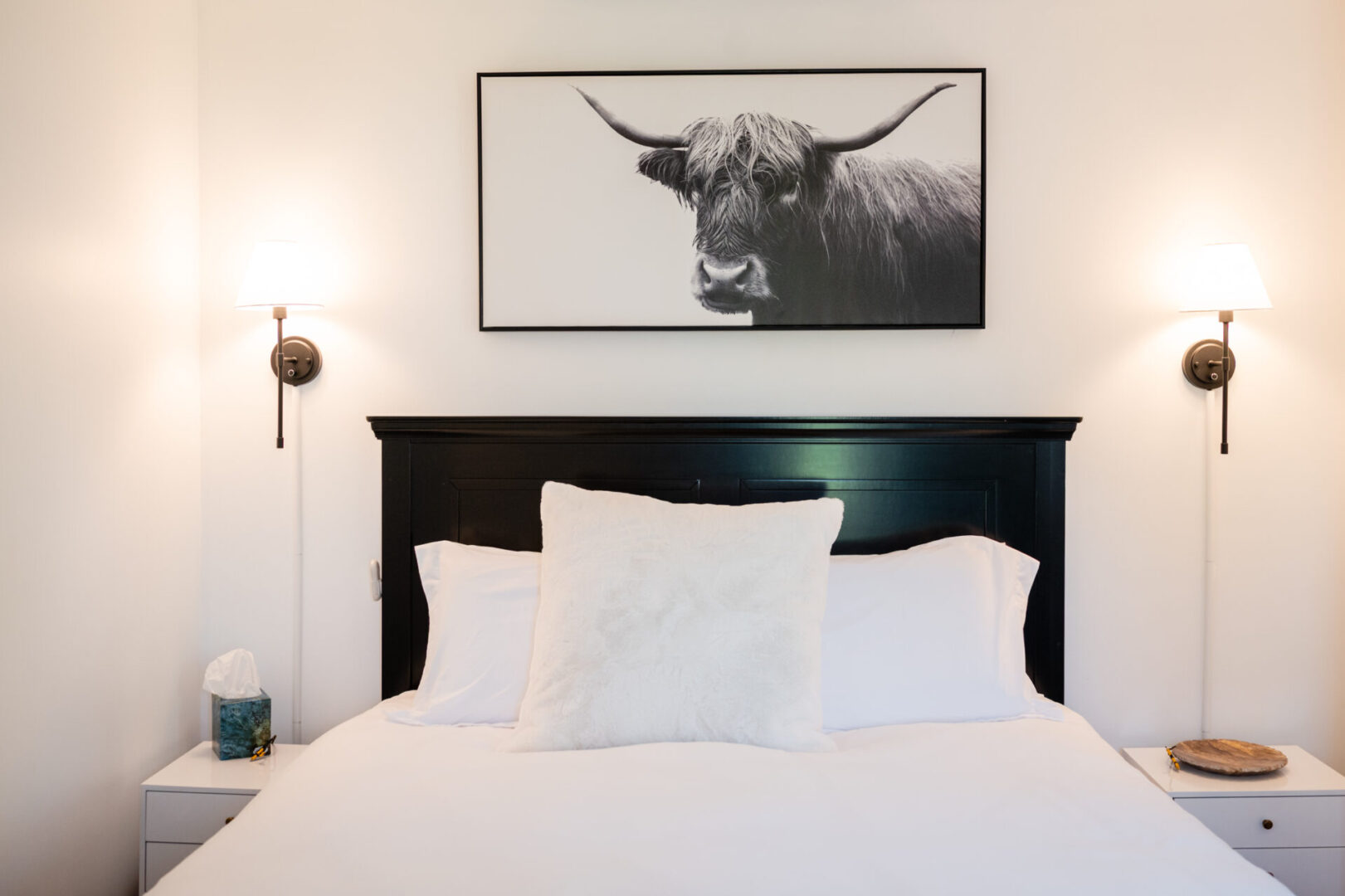 A black and white photo of a bull on the wall above a bed.