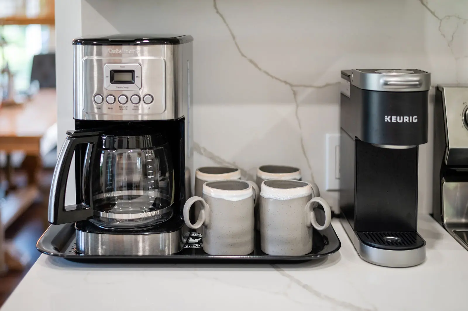 A coffee maker and two cups on a tray.